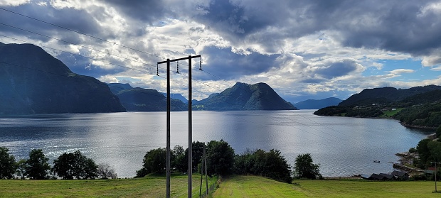 Scenic view of a Scandinavian fjord in Norway, with scenic mountains under a cloudy sky, featuring a power line in the foreground.