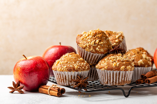 Cinnamon streusel apple muffins or mini cakes on a baking tray. Homemade bakery. Fresh red apples. Healthy breakfast. Beige background.