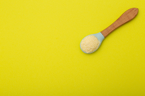 Dairy-free wheat porridge with pumpkin in a spoon on a yellow background. The concept of feeding a baby vitamin-mineral cereals for health and strengthening the immune system.