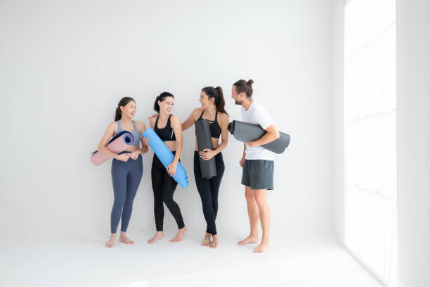 un grupo de atletas femeninos y masculinos se pararon y charlaron amistosamente en el estudio antes de comenzar con la clase de yoga. - amicably fotografías e imágenes de stock