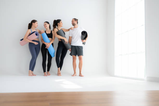 eine gruppe von sportlerinnen und sportlern stand und plauderte freundschaftlich im studio, bevor es mit der yogastunde begann. - amicably stock-fotos und bilder