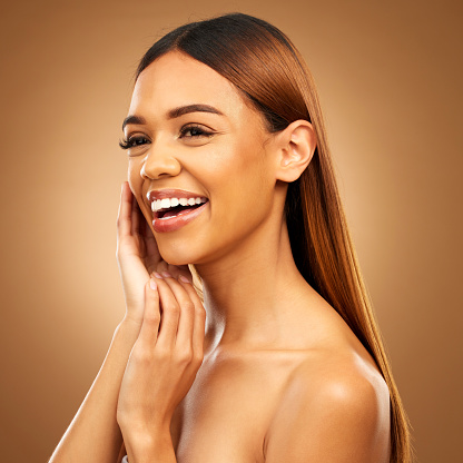 Woman with hand on face, smile and skincare with bronze glow and luxury salon treatment on brown background. Beauty, makeup and skin care cosmetics, hispanic model with straight hair style in studio.