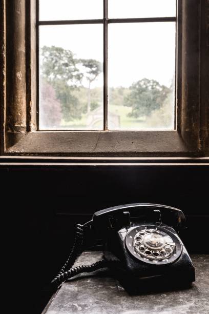 un vieux téléphone se trouve devant une fenêtre avec un cadre brun - side table table antique classic photos et images de collection