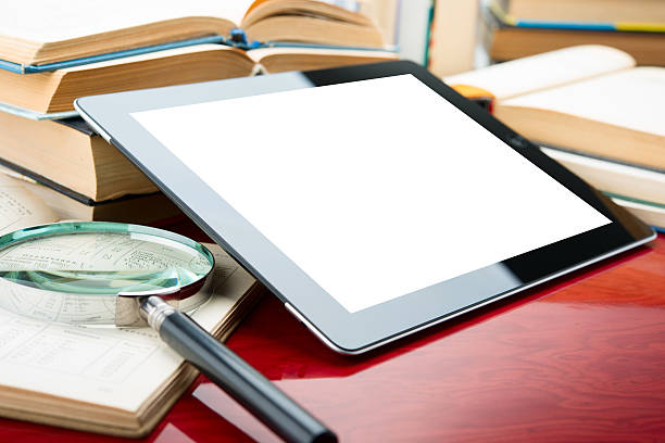 Digital tablet next to magnifying glass and opened books stock photo