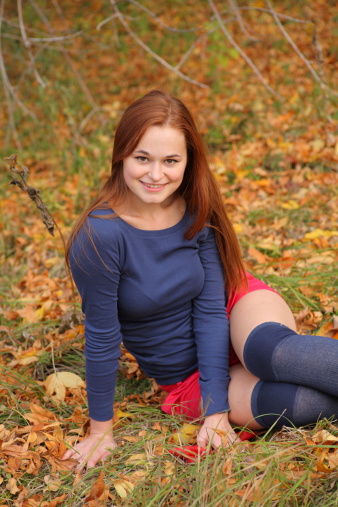 romantic redhead girl sitting in autumn leaves