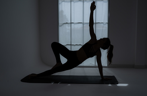 Silhouette of a young woman practicing yoga in the room.