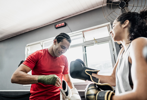 Instructor and student putting boxing gloves at gym