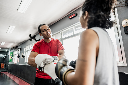 Instructor and student putting boxing gloves at gym