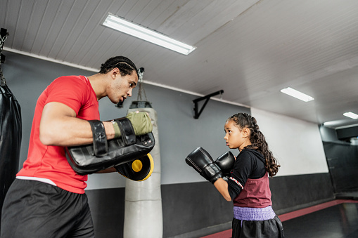 Child girl practicing boxing or muay thai with instructor at gym