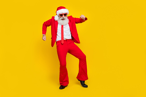 Full length photo of good mood man pensioner dressed red suit santa hat dancing empty space isolated yellow color background.