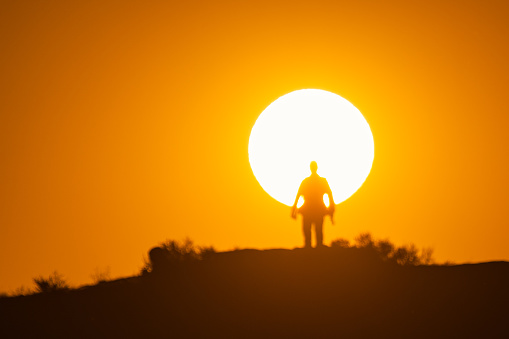 As the sun rises, a male photographer opens his silhouette standing on the mountain