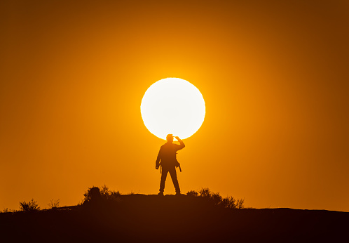 As the sun rises, a male photographer opens his silhouette standing on the mountain