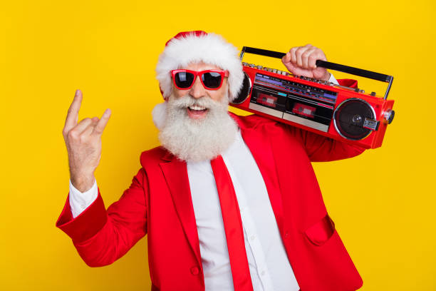 Photo of cool attractive santa dressed red suit tie enjoying boom box songs showing hard rock sign isolated yellow color background Photo of cool attractive santa dressed red suit tie enjoying boom box songs showing hard rock sign isolated yellow color background. punk santa stock pictures, royalty-free photos & images