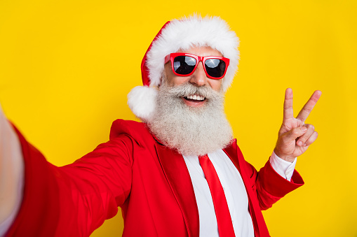 Photo of handsome cool santa dressed red suit tie showing v-sign recording video vlog isolated yellow color background.