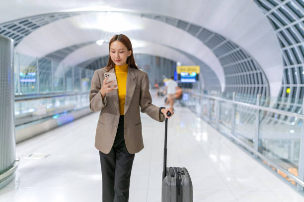 istock Young Asian businesswoman carrying suitcase using smartphone while walking to her boarding gate for her flight at the airport departure terminal. Young asian woman on business trip. Young Woman business on the move. Digital banking anytime, anywhere. 1791153917