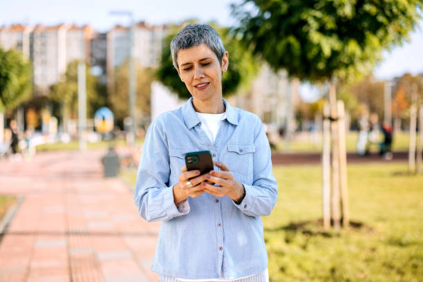 istock Smiling mature woman using phone at public park 1791157781