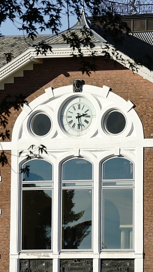 viken, Norway – October 14, 2023: A close-up shot of a clock face affixed to the exterior wall of a large building, with the reflection of a second clock in the window, illuminated