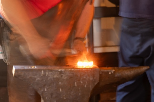 A blacksmith crafting a piece of hot glowing metal on an anvil
