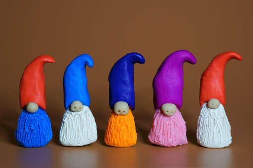 Figurines of colorful dwarfs made of plasticine. Brown background.