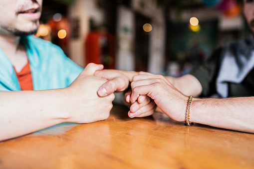 Close-up of a gay couple holding hands at restaurant