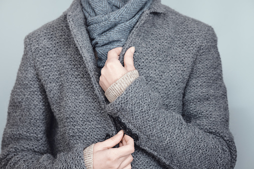 Close-up of a woman in a gray knitted jacket and blue scarf. Winter, autumn warm woolen clothes.