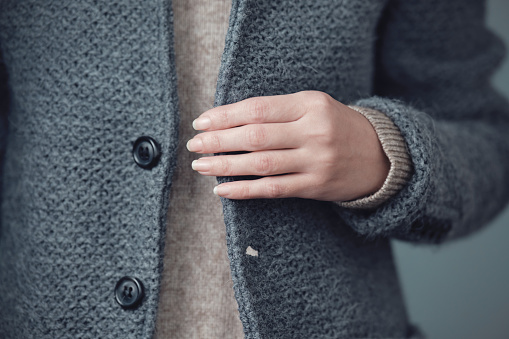 Close-up of a gray knitted jacket and a woman's hand. Winter, autumn warm woolen clothes.