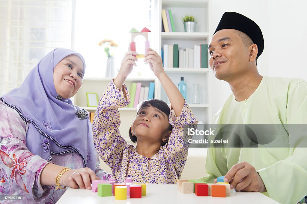 Building a wooden toy house Malay family at home. Muslim girl building a wooden toy house. Southeast Asian parents and child living lifestyle. Islam Stock Photo