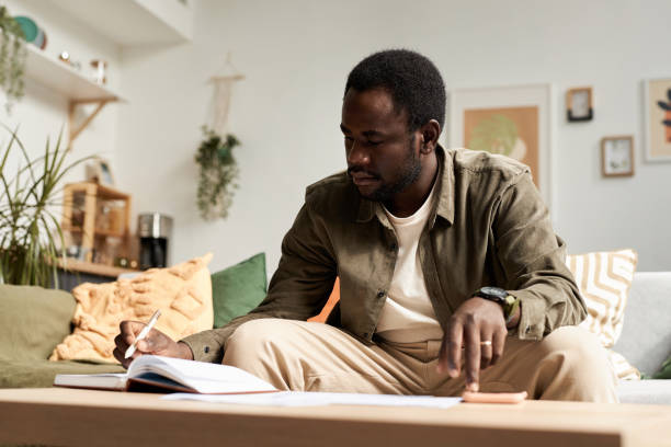 African American man writing in notebook in sunlight and doing home finances