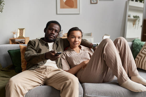 Young African American couple watching Tv together and holding remote