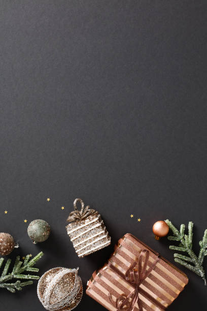 istock Elegant Christmas vertical composition with luxury gift box, bronze balls, and confetti on black background create a festive atmosphere. Modern design for holiday cards, posters, and invitations 1791205152