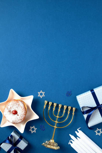 Blue background with festive Hanukkah composition. Menorah, gift boxes, candles, jelly donuts on blue table. Traditional Jewish holiday celebration. Chanukah greeting card concept stock photo