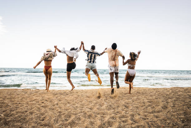 A happy-go-lucky group of friends take a jump shot at the beach. Exhibiting freedom and glee, this group of friends create a sense of joy and adventure. The sunset glows behind them.