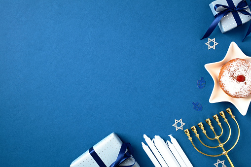 Hanukkah celebration photo with festive menorah, sufganiyot, candles, and gift boxes on a blue background. Perfect for holiday card, banner, or invitation. Jewish culture and tradition composition