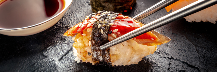 Sushi with chopsticks and soy sauce panorama. Unagi sushi, nigiri with eel, on a black background. Japanese restaurant