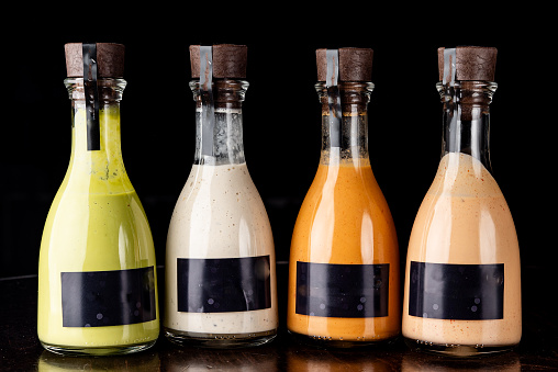 Set of glass bottles with different delicious craft sauces on black background