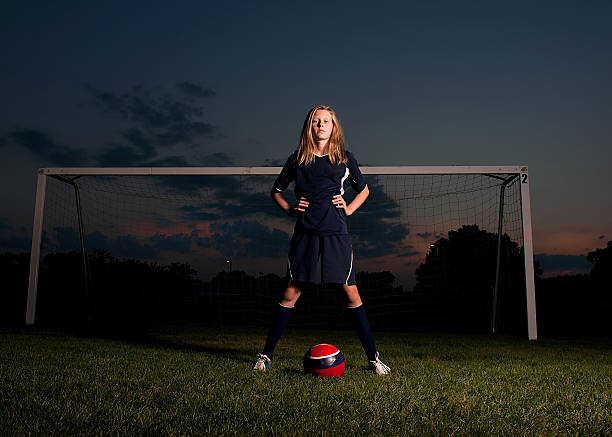 Soccer Player at Sunset Girl in soccer uniform with ball standing in front of goal in the dark at sunset womens soccer stock pictures, royalty-free photos & images