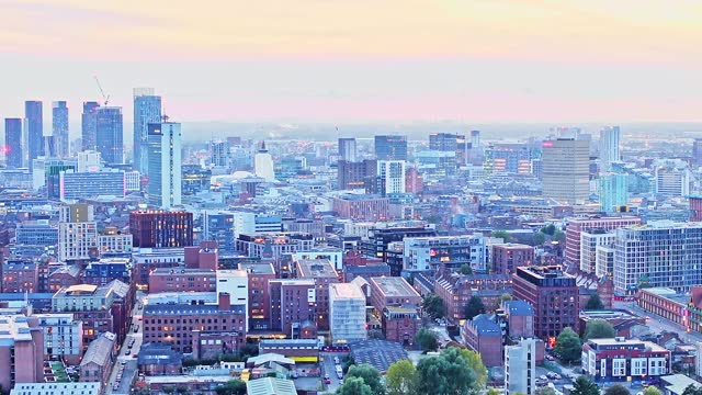 Zoomed drone lifting shot of the illuminated skyline of Manchester after sunset.