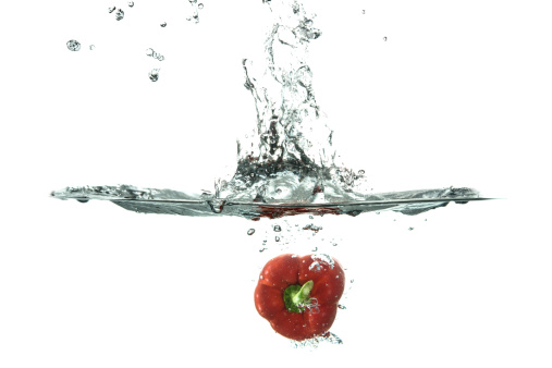 raw vegetables splashed into water against white background