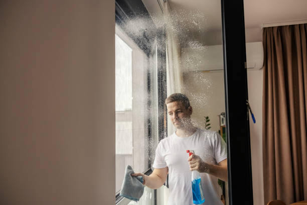 istock A happy man is spraying detergent on window glass and cleaning it while standing at home. 1791242800