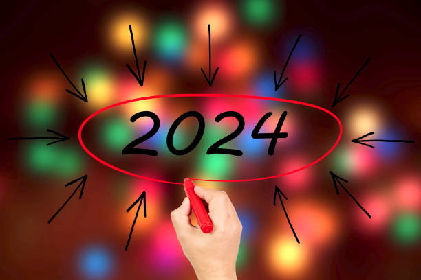 2024, Woman writing the number 2024 on background of faded lights. Happy New Year stock photo