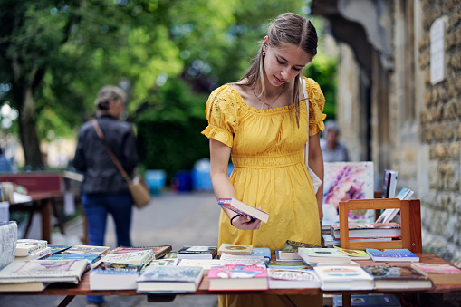 Teenage girl enjoying summer vacations in Gloucestershire, United Kingdom. 
She is walking in the beautiful village of Bourton-on-the-Water. The girl is browsing books in a charity street market.
Shot with Canon R5