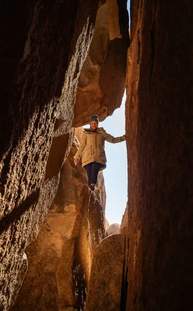 Female hiker standing on a very narrow cliff among rock formations in California's Hall of Horrors, Joshua Tree National Park