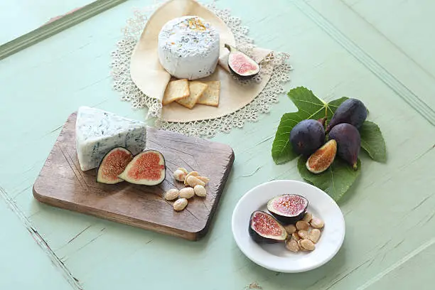 Fresh figs adorned around a a variety of organic cheeses and marcona almonds, natural light on aged wood.