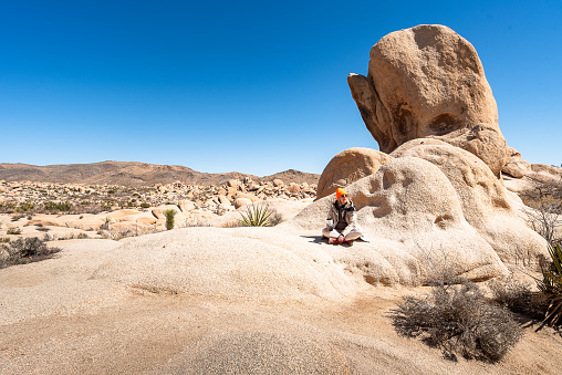 Female traveler enjoying in journey and freedom while sitting on a large sunlit rock in Joshua Tree National Park, California