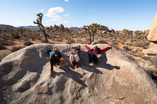 Three friends enjoying in journey and freedom while lying and resting on a large sunlit rock in Joshua Tree National Park, California
