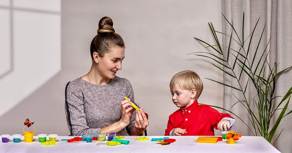 The child, together with his mother, sculpts figurines from plasticine and plays merrily. A little boy is learning to sculpt various figures from plasticine. Educational toys for children.