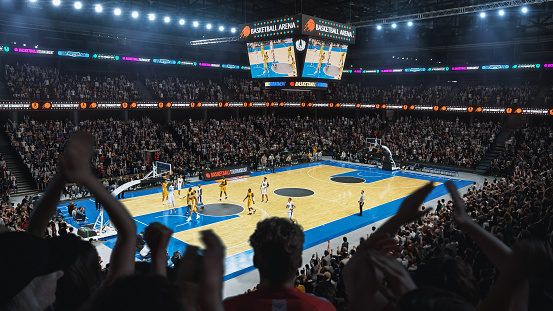High Angle Establishing Wide Shot of Whole Arena of Spectators Watching a Basketball Championship Game. Teams Play, Crowds of Fans Raise Hands and Cheer. Sports Channel Live Television Broadcast