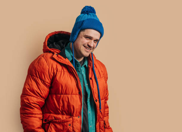 istock Funny caucasian guy in blue hat, orange down jacket on brown background 1791326972