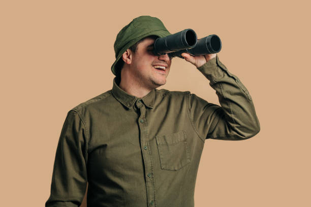 istock Stylish guy in boonie hat with binoculars on brown background 1791329244