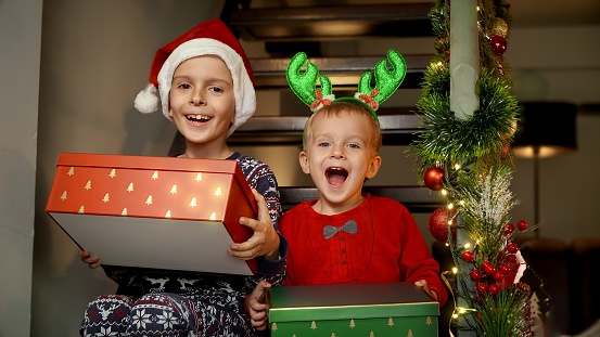 Two cheerful laughing boys wearing pajamas holding gifts and presents from Santa. Family celebrations on winter holidays